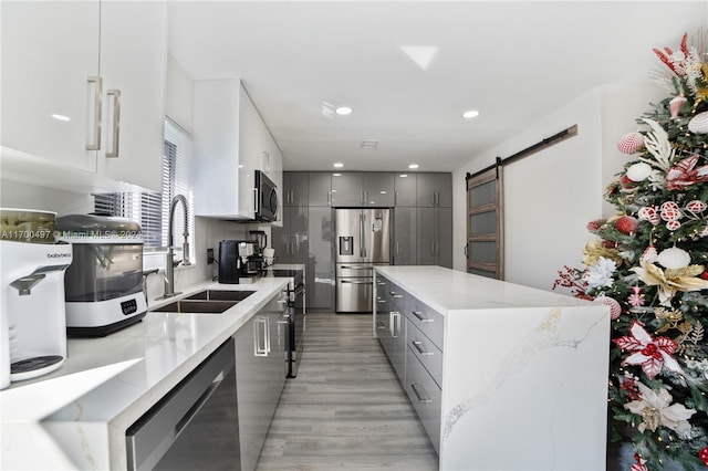 kitchen featuring gray cabinetry, sink, stainless steel appliances, a barn door, and light wood-type flooring