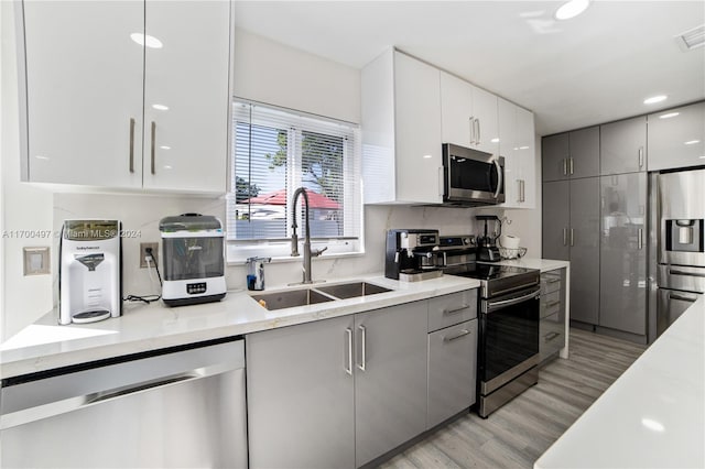 kitchen with light hardwood / wood-style floors, stainless steel appliances, sink, gray cabinets, and white cabinetry