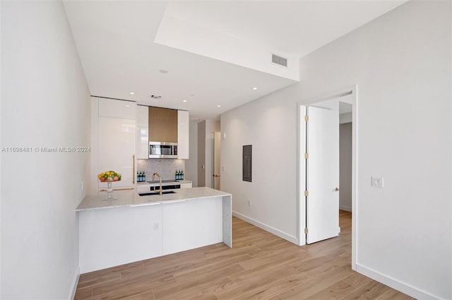 kitchen featuring kitchen peninsula, backsplash, sink, light hardwood / wood-style floors, and white cabinetry