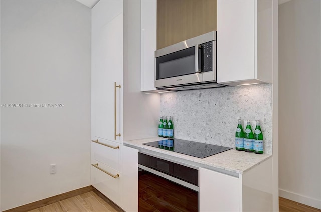 kitchen featuring black electric stovetop, decorative backsplash, wall oven, light hardwood / wood-style floors, and light stone counters