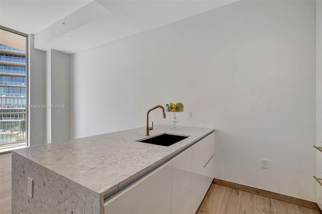 kitchen featuring kitchen peninsula, white cabinetry, sink, and light wood-type flooring