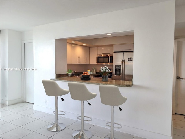 kitchen featuring kitchen peninsula, cream cabinets, a breakfast bar area, light tile patterned floors, and appliances with stainless steel finishes