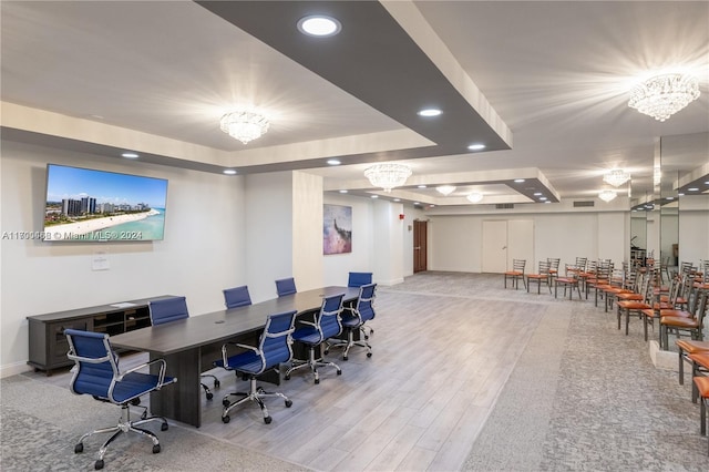 office space with a raised ceiling, light wood-type flooring, and an inviting chandelier