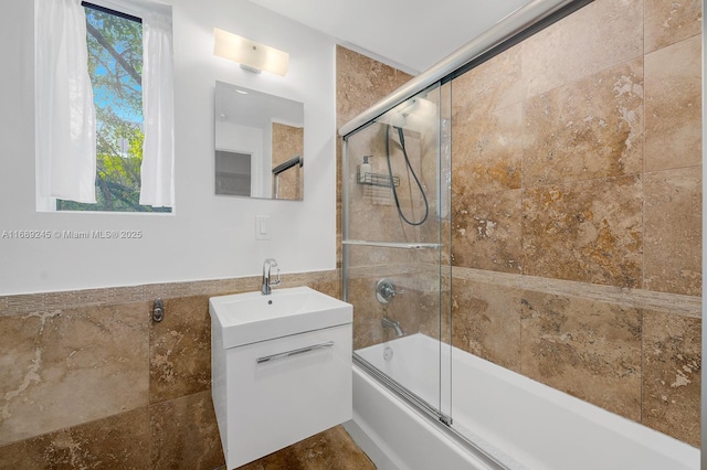 full bath featuring tile walls, bath / shower combo with glass door, vanity, and a wainscoted wall