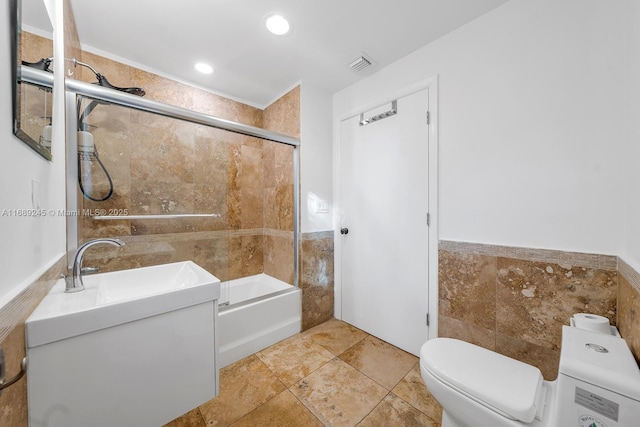full bath featuring visible vents, tile walls, wainscoting, bath / shower combo with glass door, and toilet