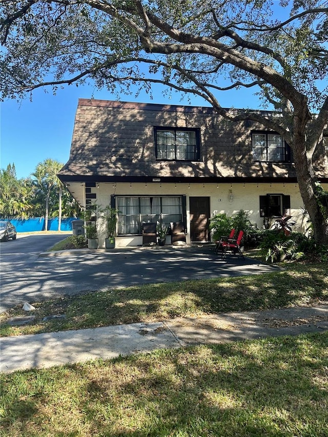 view of front of house with a water view, a patio area, mansard roof, and stucco siding