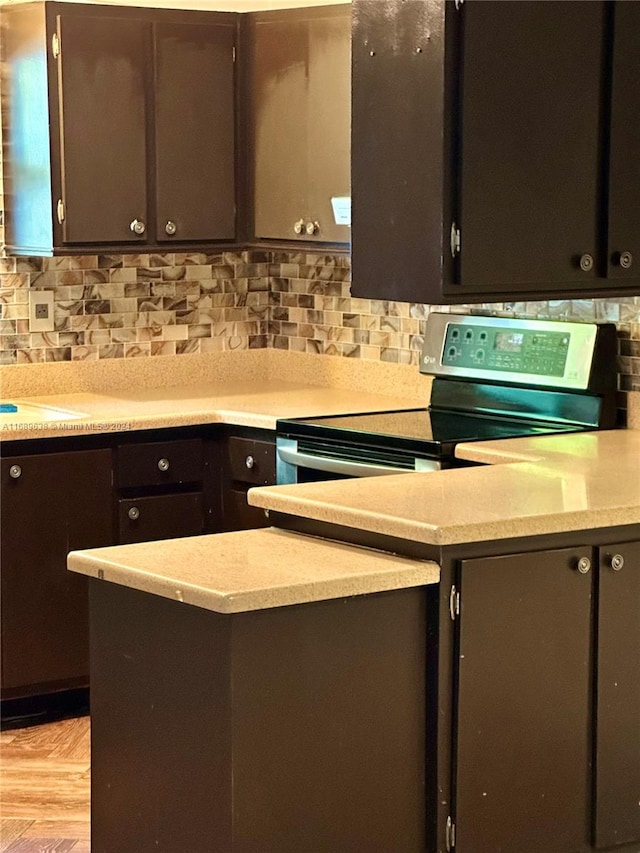 kitchen with electric range, light hardwood / wood-style floors, dark brown cabinetry, and tasteful backsplash