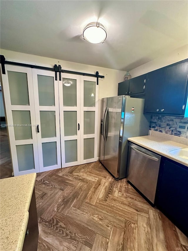 kitchen with a barn door, blue cabinets, stainless steel appliances, and parquet flooring