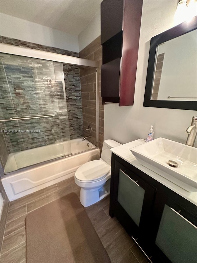 full bathroom with combined bath / shower with glass door, vanity, and toilet