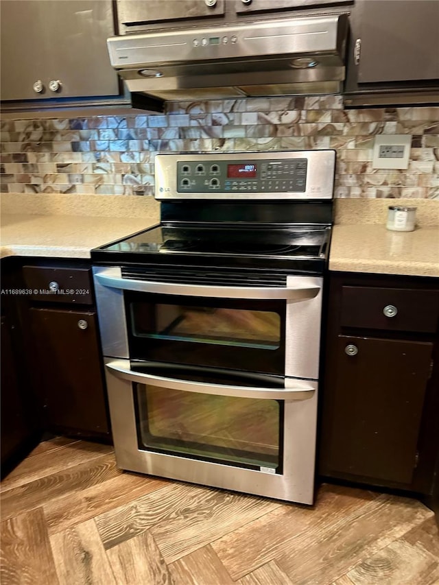 kitchen featuring decorative backsplash, dark brown cabinetry, ventilation hood, and stainless steel electric range oven