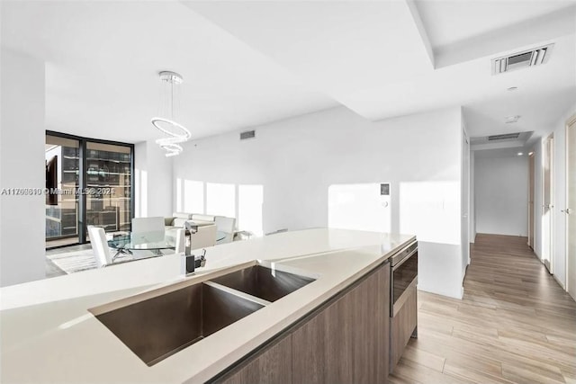 kitchen with pendant lighting, light hardwood / wood-style floors, a notable chandelier, and sink