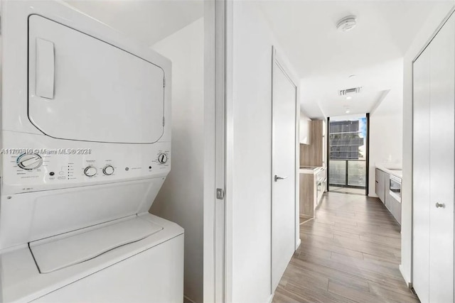 washroom with stacked washer and dryer and light hardwood / wood-style floors