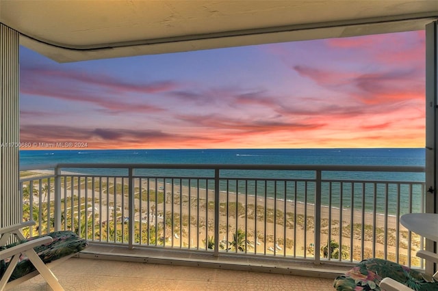 balcony at dusk featuring a water view and a beach view