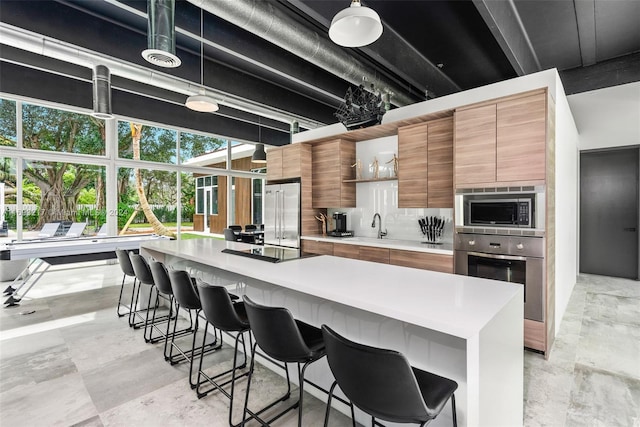 kitchen featuring a center island, backsplash, sink, built in appliances, and a kitchen bar