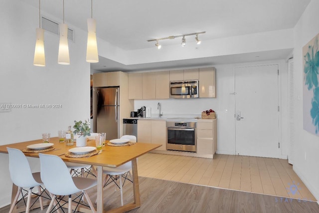 kitchen with appliances with stainless steel finishes, sink, decorative light fixtures, light hardwood / wood-style flooring, and cream cabinetry