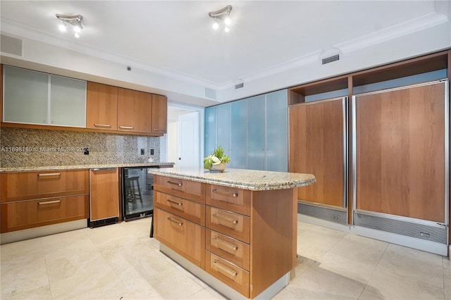 kitchen with decorative backsplash, light stone counters, beverage cooler, crown molding, and a center island