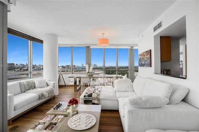 living room with floor to ceiling windows, wood finished floors, visible vents, and a city view