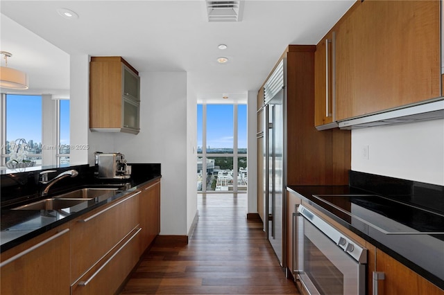 kitchen featuring floor to ceiling windows, brown cabinetry, a sink, and oven