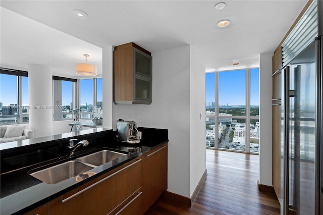 kitchen with dark countertops, dark wood-style flooring, a view of city, stainless steel built in refrigerator, and a sink