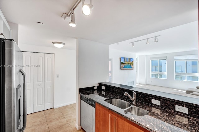 kitchen featuring track lighting, stainless steel appliances, light tile patterned floors, sink, and dark stone countertops