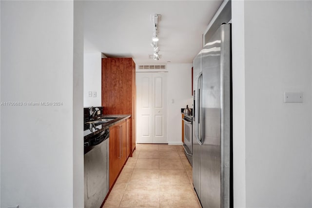 kitchen with appliances with stainless steel finishes, sink, rail lighting, and light tile patterned floors