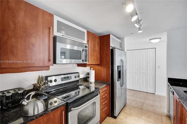 kitchen featuring light tile patterned floors, track lighting, stainless steel appliances, and dark stone countertops