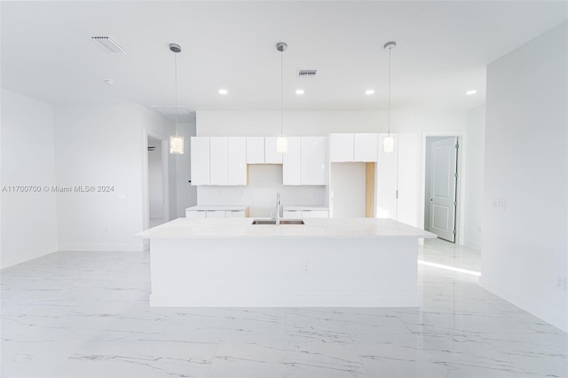 kitchen featuring white cabinets, decorative light fixtures, sink, and an island with sink