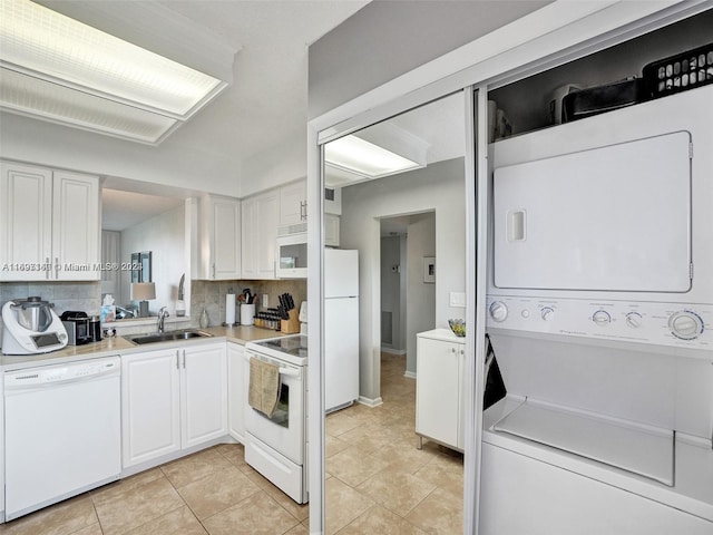 kitchen featuring white appliances, sink, stacked washer and dryer, tasteful backsplash, and white cabinetry