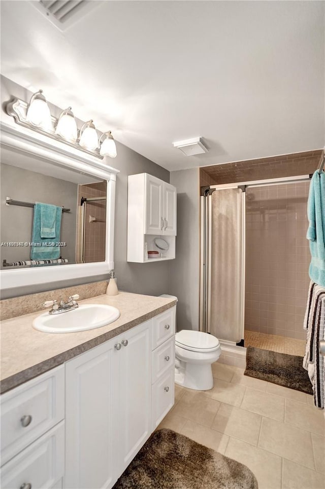 bathroom featuring tile patterned flooring, vanity, toilet, and tiled shower