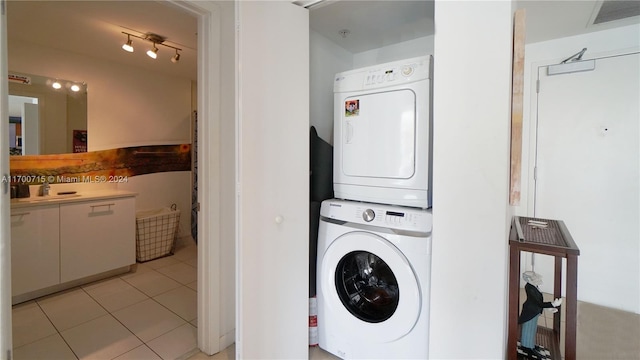 laundry area with sink, light tile patterned flooring, and stacked washer and clothes dryer