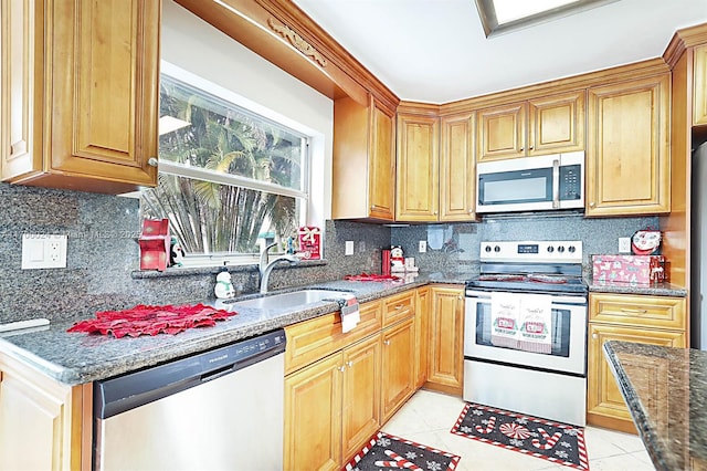 kitchen with sink, dark stone counters, light tile patterned floors, and appliances with stainless steel finishes