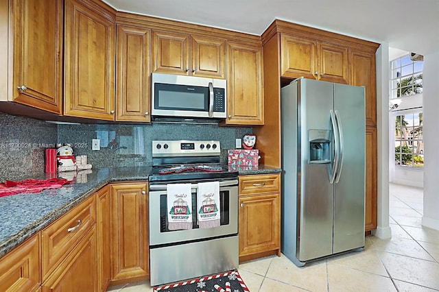 kitchen with light tile patterned floors, decorative backsplash, dark stone counters, and stainless steel appliances