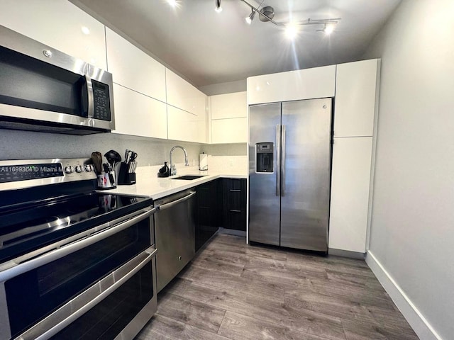 kitchen featuring hardwood / wood-style floors, track lighting, white cabinets, sink, and appliances with stainless steel finishes