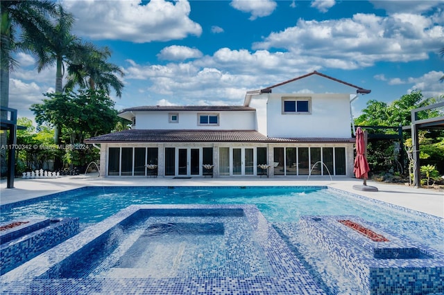 back of property with a swimming pool with hot tub, pool water feature, and a patio area