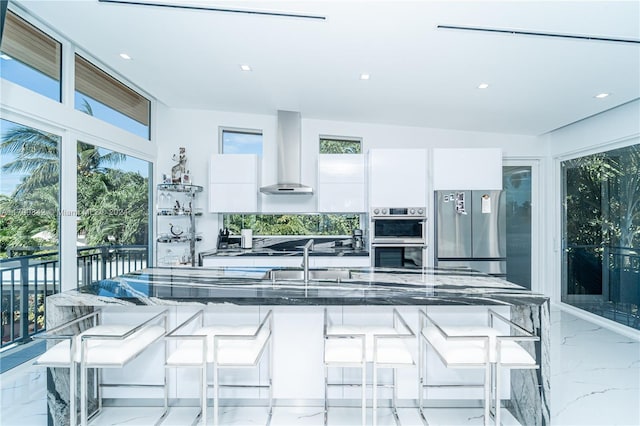 kitchen with wall chimney exhaust hood, white cabinetry, a breakfast bar area, and appliances with stainless steel finishes