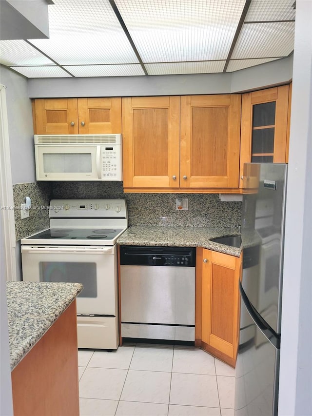 kitchen with decorative backsplash, white appliances, stone countertops, and light tile patterned flooring