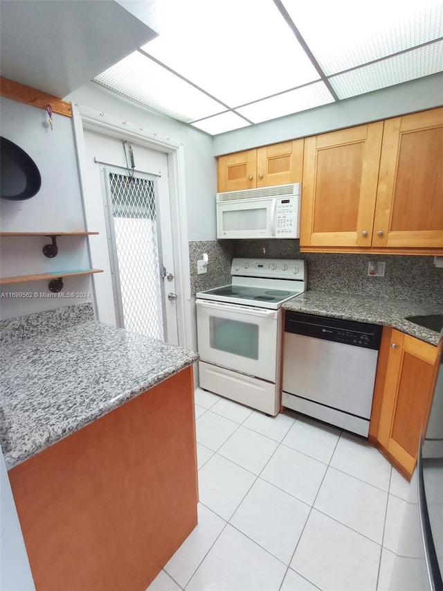 kitchen with tasteful backsplash, light tile patterned floors, stone countertops, and white appliances