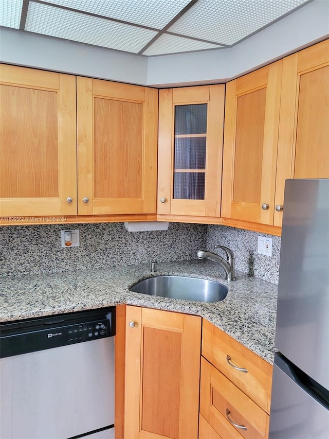 kitchen with backsplash, stainless steel appliances, light stone counters, and sink