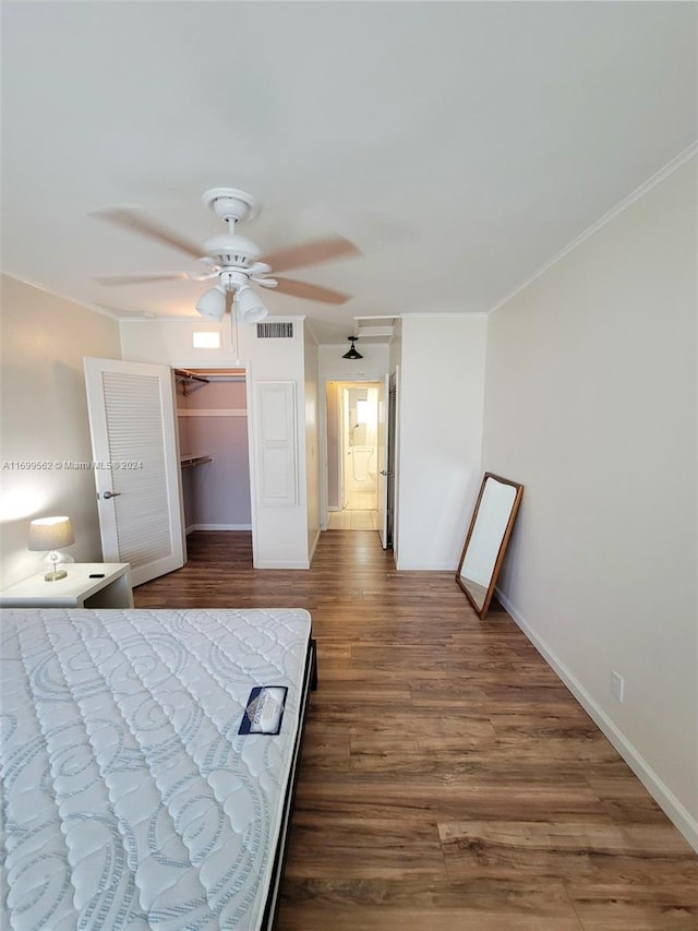 bedroom with a walk in closet, ceiling fan, crown molding, hardwood / wood-style flooring, and a closet