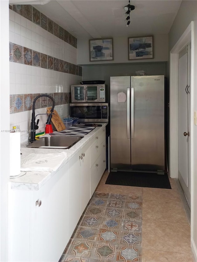 kitchen featuring appliances with stainless steel finishes, tasteful backsplash, sink, light tile patterned floors, and white cabinets