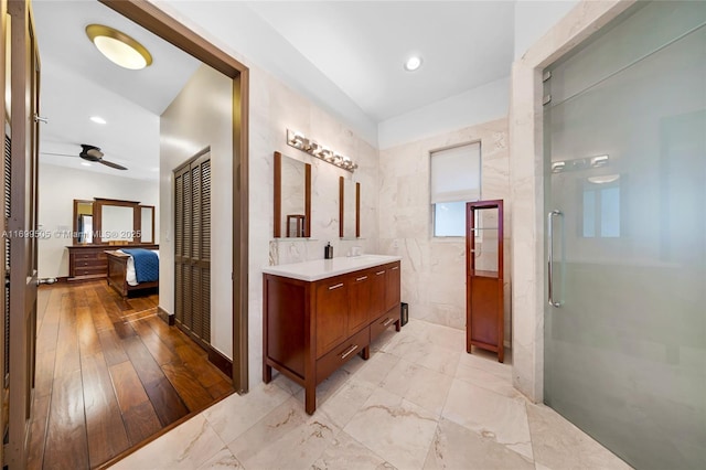 bathroom with vanity, ceiling fan, tile walls, and walk in shower