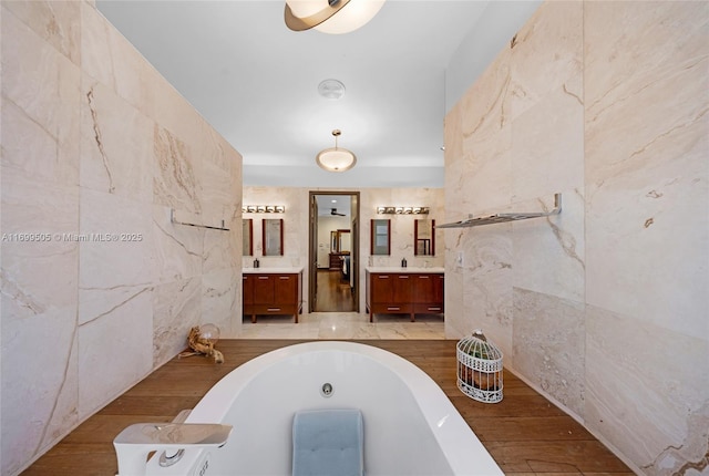 bathroom with tile walls, a relaxing tiled tub, and vanity