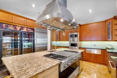 kitchen featuring backsplash, a center island, island exhaust hood, built in appliances, and light stone counters