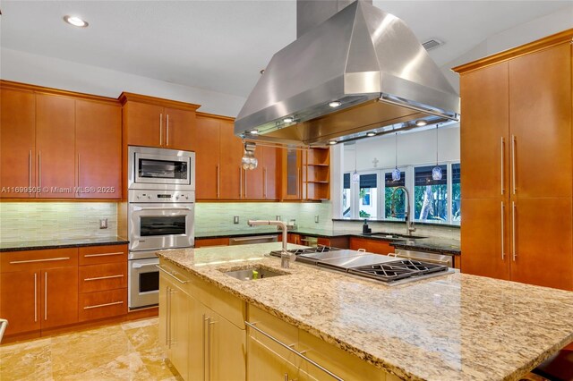 kitchen featuring an island with sink, appliances with stainless steel finishes, light stone countertops, and island range hood