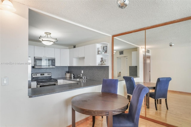 kitchen with backsplash, light hardwood / wood-style flooring, appliances with stainless steel finishes, white cabinetry, and kitchen peninsula