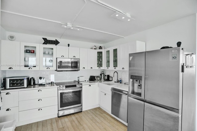 kitchen with backsplash, white cabinets, sink, light wood-type flooring, and stainless steel appliances