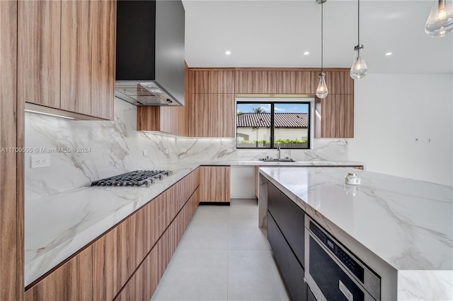 kitchen featuring light stone counters, pendant lighting, wall chimney range hood, and stainless steel gas stovetop