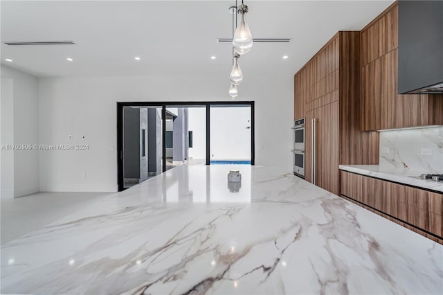 kitchen featuring light stone counters, stainless steel double oven, hanging light fixtures, and gas cooktop