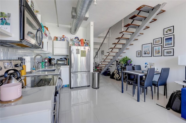 kitchen with appliances with stainless steel finishes, tasteful backsplash, sink, light tile patterned floors, and white cabinets