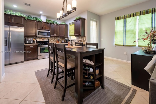 kitchen with appliances with stainless steel finishes, backsplash, dark brown cabinetry, hanging light fixtures, and light tile patterned flooring